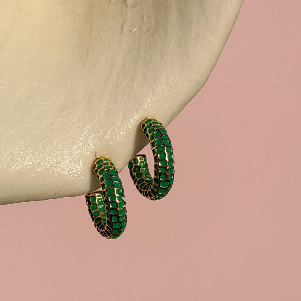Green hoop earrings on a beige surface with a pink background