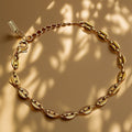 Gold chain bracelet on a beige background with leaf shadows