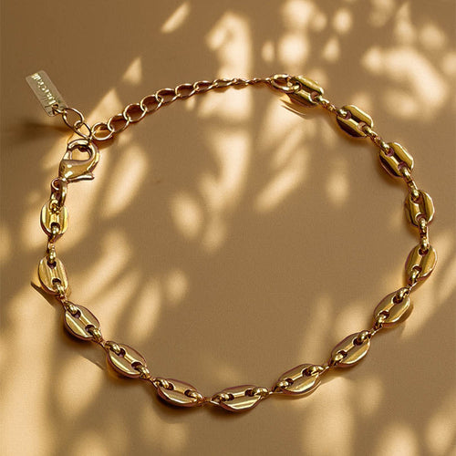 Gold chain bracelet on a beige background with leaf shadows