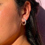 Close-up of an ear wearing a silver hoop earring with a pink background