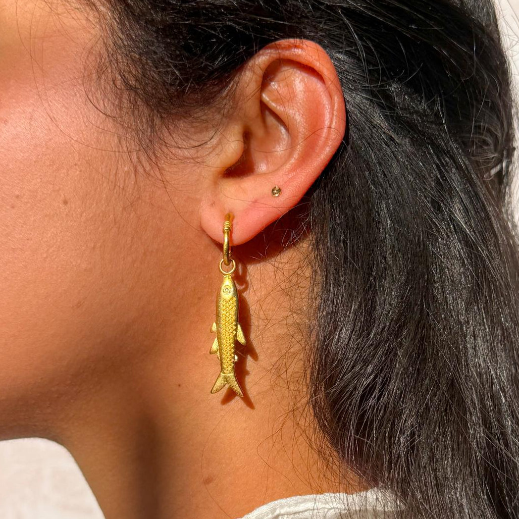 Close-up of a person wearing a gold earring with a fish design.