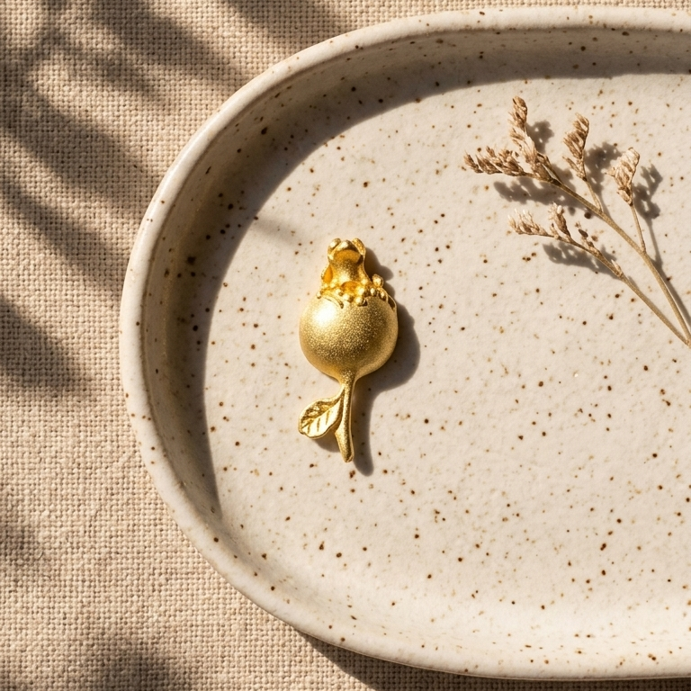 Gold decorative object on a beige speckled plate with dried plants, on a textured beige surface.