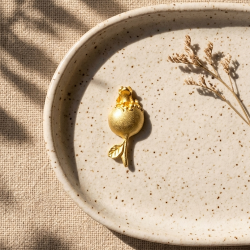 Gold decorative object on a beige speckled plate with dried plants, on a textured beige surface.